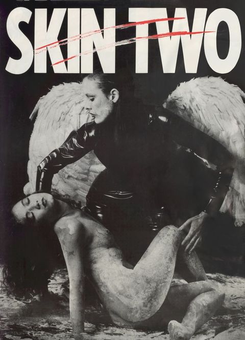 Poster. A person dressed in fitted, black patent leather clothing wears large white angel wings. They kneel down to lift the reclining body of another person who is naked and covered in a white, paint-like substance. Above them white text reading ‘SKIN TWO’ is scored across with two red, horizontal slashes.