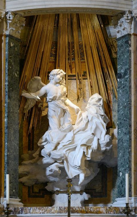 Sculpture. Carved from marble, a woman falls backwards with arms and legs spread out in submission. An angel stands over her holding a spear aimed at her heart. Carved fabric ripples around them, forming billowing waves that unite them into a single entity. 