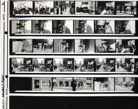 Black and white photograph. Series of 29 images on a contact sheet with protestors and police in a London street. Many feature a large banner with the text "NEWHAM 7" at the top and "Innocent" underneath. A banner is lifted behind a group of South Asian protestors raising their arms in the top-left image, which has been circled with blue ink.